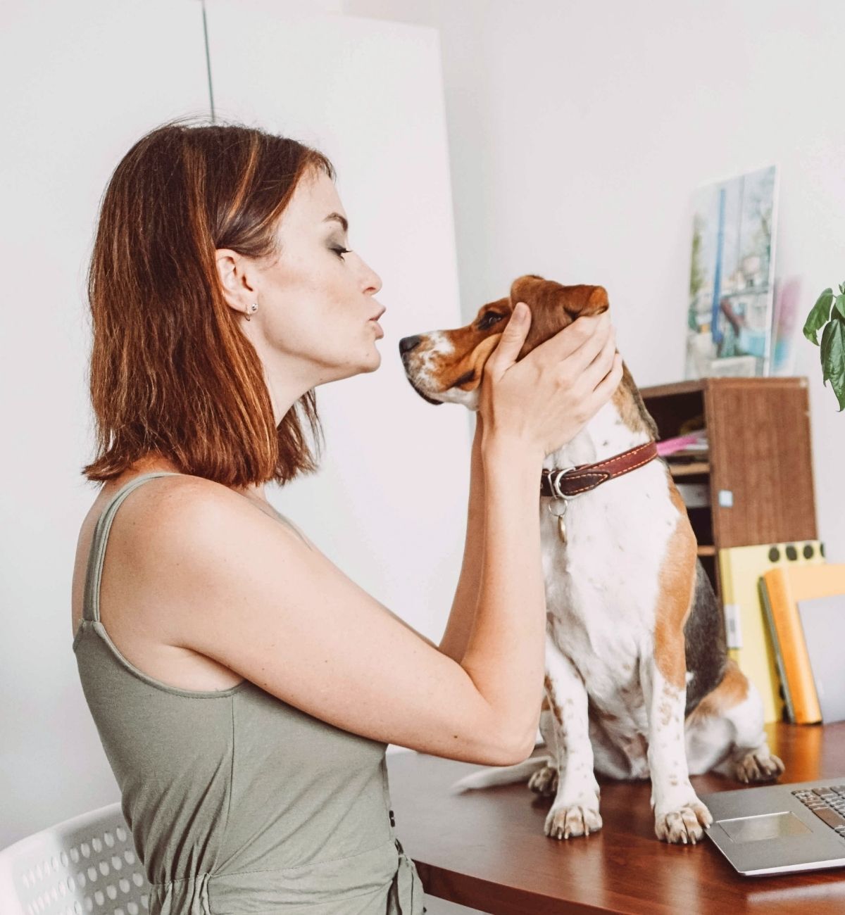 woman kissing her dog while working on her laptop